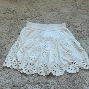 Vit broderad kjol från Zara - Supersöt vit kortkjol från Zara med broderade blommor och snygg scallop-kant. Kjolen har resår i midjan för skön passform och är gjord i mjuk bomull. Perfekt för varma dagar och ger en fräsch och somrig vibe. Passar xs, jätte bra skick! Finns inte att köpa längre
