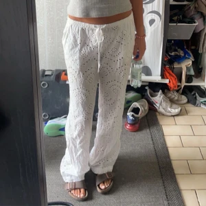Vita linnebyxor med broderade detaljer - Säljer ett par vita linnebyxor med snygga broderade hålmönster och snörning i midjan. Byxorna har en loose passform och är perfekta för varma dagar. De är midwaist och har en chill, avslappnad vibe som passar till sandaler eller sneakers.