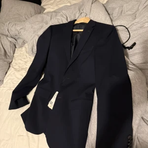 Mörkblå kavaj från H&M, strl 46/ S slimfit - Snygg mörkblå kavaj från H&M i klassisk modell med två knappar framtill. Storlek 46/S slimfit orginalpris 799kr. Helt ny
