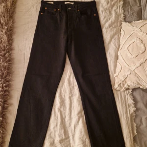 Levi's Wedgie Straight svarta jeans - Svarta Levi's Premium Wedgie Straight jeans med klassisk femficksdesign och raka ben. Hög midja och snygga nitar i kopparfärg. Jeansen är gjorda i robust denim och har den ikoniska röda Levi's-taggen bak. Perfekt för dig som gillar en clean och tidlös look. På ena fickan finns nån liten bleknings fläck (se på en av bilderna) men annars bra skick 