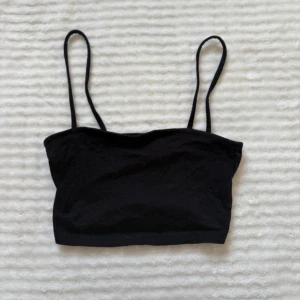 Svart bandeau topp från H&M Divided - Svart bandeau topp från H&M Divided med smala axelband. Enkel och stilren design som är perfekt för att bygga lager eller bära som den är. Mjuk och stretchig bomull som sitter skönt mot kroppen. Passar dig som gillar minimalistisk stil.