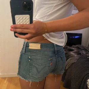 Levi's låga jeansshorts med fransar - Snygga låga jeansshorts från Levi's i klassisk blå denim. Modellen är tight och har råa, fransiga kanter samt femficksdesign och knappgylf. Perfekta för sommaren och ger en avslappnad vibe.