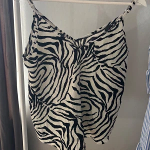 Zebramönstrad linnetopp med v-ringning - Snygg linnetopp med svartvitt zebramönster och v-ringad hals. Tunt, luftigt material och smala justerbara axelband. 