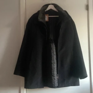 Svart kappa i kashmir och ull - Snygg svart kappa med klassisk rak passform, tillverkad i en lyxig blandning av kashmir och ull. Fodret har quiltade detaljer och kragen är mjuk och stilren. Perfekt för dig som vill ha en tidlös och elegant look. Stl 3 vilket motsvarar L samt M