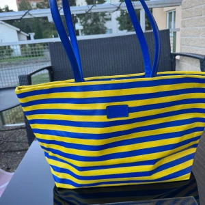 Ny Randig shoppingväska / bag - Ny stor väska med blå och gula ränder. Väskan har två rejäla handtag och en praktisk fack med dragkedja på baksidan. Perfekt för att bära med sig allt man behöver under dagen. Väskan har magnetlås. Finns på Hägerstensåsen i Stockholm. 