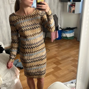 Glittrig kortklänning med zigzagmönster - Säljer en glittrig kortklänning från Pernilla Wahlgren collection i modellen. Wavy Gold Dress, med lång ärm och rund hals. Klänningen har ett coolt zigzagmönster i guld, blått, svart och beige. Materialet är glansigt och känns festligt, med en slim passform som sitter snyggt på kroppen. Perfekt för dig som gillar att sticka ut.