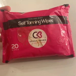 Cocoa Brown Self Tanning Wipes - Sjukt smidiga brun-utan-sol-servetter från Cocoa Brown, perfekt för både ansikte och kropp. Paketet innehåller mer än hälften wipes som ger en jämn och naturlig solbrun ton. Förpackningen är starkt rosa med svart och vitt tryck, enkel att ta med i väskan.
