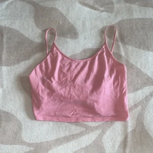 Rosa croppad linnetopp med smala band - Säljer en ljusrosa croppad linnetopp med smala axelband. Toppen har en enkel och clean design med rundad halsringning och ärmlös passform. Perfekt för varma dagar och enkel att matcha med jeans eller shorts.