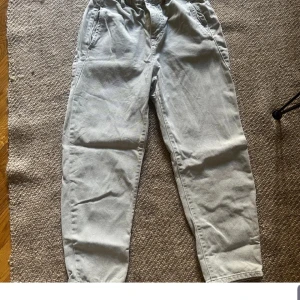 Beige tapered byxor från Zara - Snygga beige byxor från Zara med tapered passform och elastisk midja. Byxorna har praktiska sidofickor, knapp och dragkedja framtill. Perfekta för en chill och stilren look, tillverkade i mjukt bomullsmaterial som är skönt att bära hela dagen.