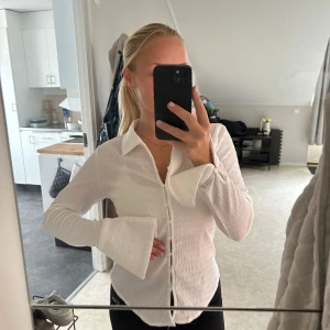 Vit skjorta med vida ärmar från Bik Bok - Säljer en vit skjorta/blus från Bik Bok i storlek S. Skjortan/ blusen har en krage, knappar framtill och är tillverkad i ett strukturerat bomullstyg. Ärmarna är långa och har extra vida muddar💕