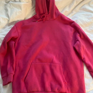 Röd hoodie med konsttryck INTENSE FEELINGS - Säljer en skrikrosa hoodie med stor ficka framtill och huva med snörning. På ryggen finns ett coolt konsttryck med texten INTENSE FEELINGS och en staty med ögonen täckta. Storlek M men känns som en L