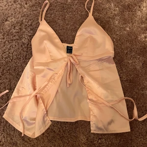 Ljusrosa omlottopp från SHEIN - Supersöt ljusrosa omlottopp från SHEIN i glansigt satinliknande material. Topp med smala axelband, djup v-ringning och knytband framtill. Perfekt för dig som gillar en feminin och trendig look.