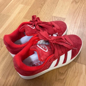 Adidas Campus röda sneakers - Säljer ett par Adidas Campus sneakers i rött mocka med vita klassiska stripes på sidorna och vit logga på tungan. Skorna har rund tå, platt sula och breda röda snören. Perfekt för dig som gillar retrostil och vill sticka ut med färg. Storlek 37 1/3. HELT NYA BARA ANVÄNT EN GÅNG!!  Köpt för 1300kr