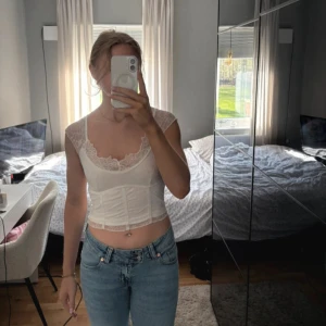 Vit spetskorsett croppad topp - Säljer en vit croppad korsett-topp med spetsdetaljer och korta ärmar. Toppen har en figurnära passform, markerad midja och vacker spets längs halsringningen och axlarna. Perfekt för dig som gillar romantisk och trendig stil.