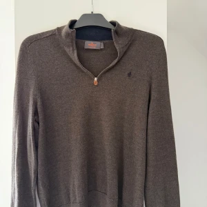 Brun merinoulltröja med half zip Morris - Snygg brun långärmad tröja från Morris i 100% merinoull. Tröjan har en stilren half zip-dragkedja vid halsen och en liten broderad logga på bröstet. Perfekt för dig som gillar klassisk och enkel stil med premiumkänsla.