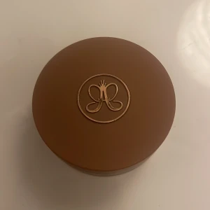 Anastasia Beverly Hills Cream Bronzer Caramel - Säljer en Anastasia Beverly Hills Cream Bronzer i färgen Caramel. Kommer i en rund brun plastburk med guldigt logotryck på locket. Formulan är krämig och lätt att blenda för en naturlig solkysst look. Vegansk och cruelty free.