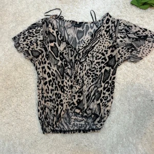Leopardmönstrad blus med v-ringning - Säljer en blus med leopardmönster i svart och beige. Blusen har v-ringning, korta ärmar 