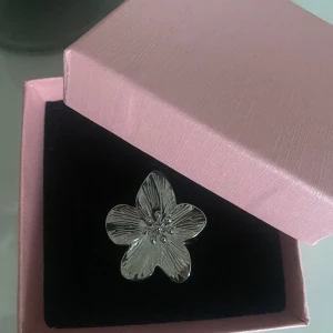 Silverring med blomformad design - Unik silverring med en stor blomformad front, detaljerade linjer och små pärlliknande detaljer i mitten. Perfekt för dig som vill sticka ut med ett statement-smycke. Kommer i en söt rosa ask.