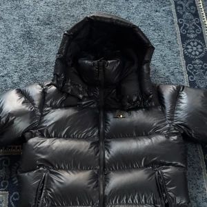 Marinblå vinterjacka från J.Lindeberg - Säljer en svart, riktigt puffig dunjacka från J.Lindeberg med 800 fill power. Har testat den ett par gånger men syns inte. Jackan har huva, dragkedja framtill och två stora fickor med dragkedja. Materialet är glansigt och känns lyxigt, perfekt för kalla vinterdagar. Stilsäker och varm, passar dig som gillar streetwear. Nypris ligger på 5.500 kr. 