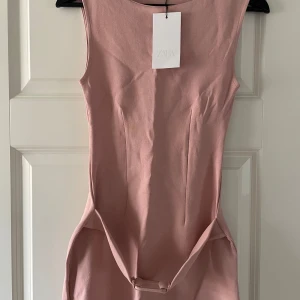 Oanvänd Rosa kort klänning från Zara - Snygg rosa kort klänning från Zara med ärmlös design och rund hals. Klänningen har en figurnära passform och ett bälte i midjan.❤️