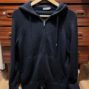 Mörkblå hoodie i kashmir från Suitsupply - Mörkblå hoodie från Suitsupply i 100% kashmir. I mycket gott skick som har mycket kvar att ge. Har en liten defekt på högra snöret men syns ej vid användning 