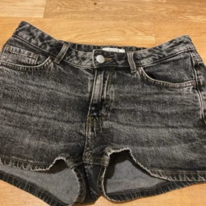 Svarta jeansshorts från Lindex - Snygga svarta jeansshorts från Lindex med tvättad look och klassisk femficksdesign. Modellen är midwaist med knapp och dragkedja framtill, samt råa kanter vid bensluten för en cool vibe. Perfekta för sommarens alla häng.