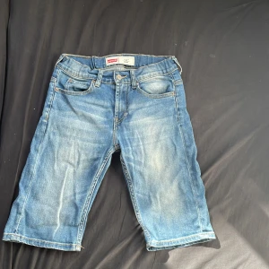 Levi's 511 Slim jeansshorts blå - Säljer ett par Levi's 511 Slim jeansshorts i klassisk blå denim. Modellen har fem fickor, knapp och dragkedja framtill samt Levi's ikoniska läderpatch bak. Snygg tvätt med lätt slitning och raka ben. Perfekt för dig som gillar en clean och tidlös look.
