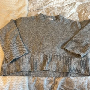 Grå stickad tröja från Gina Tricot - Mysig grå stickad tröja från Gina Tricot med breda ribbade muddar vid ärmslut och nederkant. Tröjan har en rund hals och långärmade ärmar, perfekt för att hålla värmen. Enkel och stilren design som funkar till jeans eller kjol. Nopprig därav priset 🍁🍂