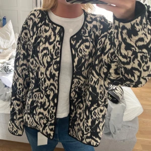 Svartvit mönstrad quiltad jacka - Säljer en svartvit quiltad jacka med leopardinspirerat mönster. Jackan har rundad hals, knäppning framtill. Modellen är loose fit och har långa ärmar. Köpt i våras, inga defekter. Storlek M men mer som en S