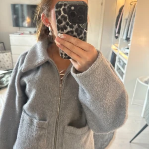Grå teddyjacka från Vila, strl 36 - Mysig grå teddyjacka från Vila i storlek 36. Jackan har dragkedja framtill, stora fickor och en bred krage. Den är lite croppad och har en loose passform med långa ärmar. Perfekt för dig som gillar en chill och trendig look.