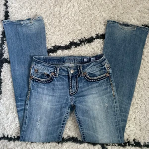 Miss me jeans - jätte Snygga ljusblå lågmidjade bootcut Miss Me jeans och coola broderade detaljer på fickorna. Jeansen har kontrastsömmar, dekorativa knappar och slitningar framtill. Midjemåttet 38 rakt över, innerbensmåttet 81cm