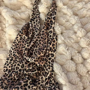 Leopardmönstrad omlottklänning - Säljer en snygg leopardmönstrad omlottklänning med djup v-ringning och axelbandslös design. Blusen  har en kort längd och är gjord i ett mjukt, glansigt material som ger en lyxig känsla. Köptes i somras i Spanien från berska endast testad enstaka gånger hemma.