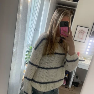 Vit stickad tröja med blå ränder - Mysig och chunky stickad tröja i vit med breda mörkblå ränder. Tröjan har en loose passform och långa ärmar, perfekt att slänga på sig när det är lite kyligt. Materialet är grovstickat och ger en skön och avslappnad vibe.