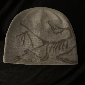Vit mössa från Arc'teryx - Snygg vit mössa från Arc'teryx med ett stilrent fågelmönster i grått. Perfekt för kyliga dagar med sin mjuka och bekväma passform. Tillverkad i högkvalitativt material för extra värme och komfort. Helt ny, säljer då jag inte har någon användning för den längre.