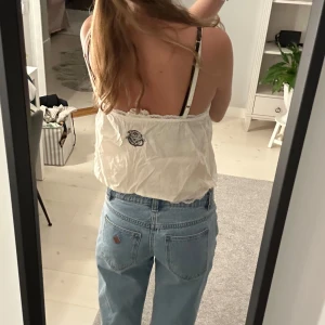 oddmolly topp - Supersöt vit linnetopp från Juicy Couture med tunna axelband, spetsdetaljer vid halsringningen och en liten vinröd rosett framtill. Toppen är croppad och har en loose passform, perfekt för sommarens alla dagar.