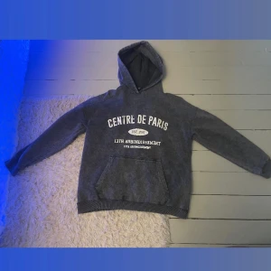Grå hoodie  - Säljer en mörkgrå hoodie från boohoo  med vit textprint på bröstet. Tröjan har huva, känguruficka och ribbade muddar vid ärmslut och nederkant. Perfekt för chill dagar eller när du vill ha en avslappnad stil.