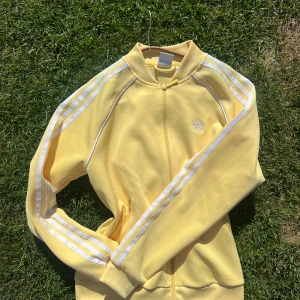 Gul Adidas tröja med dragkedja - Säljer en  gul Adidas tröja  med klassiska vita ränder längs ärmarna och broderad logga på bröstet. Fint skick! 