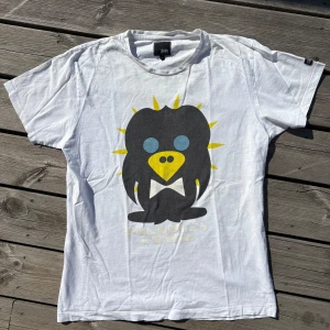 Vit t-shirt med pingvintryck Jack & Jones stl.M - Vit t-shirt från Jack & Jones med ett stort, färgglatt pingvintryck på framsidan. Trycket har svarta, gula och blå detaljer och texten 'Penguin Style' under motivet. Klassisk passform och rund hals. Perfekt för dig som gillar coola och lekfulla prints.