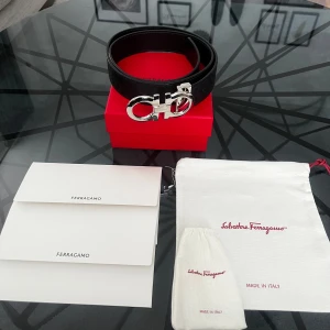 Svart Ferragamo skärp med silverdetalj - Vändbar och justerbart Gancini bälte i slätt och hamrat kalvskinn. Köptes 2024, kvitto, etiket, box, dustbag osv tillkommer. För frågor eller funderingar är det bara att skriva!!