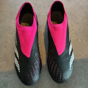 Adidas svarta och rosa fotbollsskor - Säljer ett par Adidas fotbollsskor i svart och rosa med vita detaljer. Skorna har en strumpliknande passform utan snörning och mönstrad sula med rosa dobbar för bra grepp på planen. Perfekta för dig som vill sticka ut på fotbollsplanen!