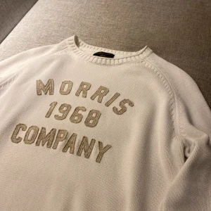 Vit stickad tröja ifrån Morris  - Snygg vit stickad tröja från Morris Gents i storlek medium. Tröjan har tryck med 'Morris 1968 Company' på bröstet och ribbade muddar vid ärmslut och nederkant. Perfekt för dig som gillar klassisk stil med en modern touch.