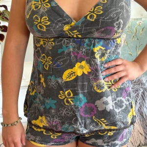 Blommig grå linnetopp från ONLY - Supersöt linne set från ONLY i grått med färgglada blommor i gult, lila, turkos och grått. Toppen har v-ringad omlottfront, tunna axelband och smockad rygg för skön passform. Perfekt för dig som gillar boho-vibes och mjuka material.