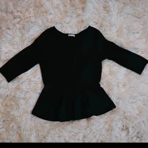Svart peplumtop med trekvartsärm - Snygg svart peplumtop från Cubus med rund hals och trekvartsärmar. Toppen har en markerad midja och volang nedtill som ger en cool siluett. Perfekt att styla med kjol eller jeans för en trendig look.