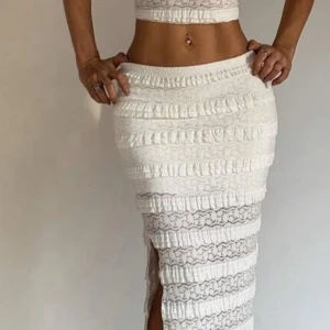 Vit långkjol med spets och volanger samt en topp till  - Supersnygg vit långkjol med spetsdetaljer och volanger i hela kjolen. Kjolen har en slits på sidan som ger en extra cool touch. Den är figurnära och passar perfekt till crop tops eller linnen. Perfekt för dig som gillar romantisk och trendig stil.