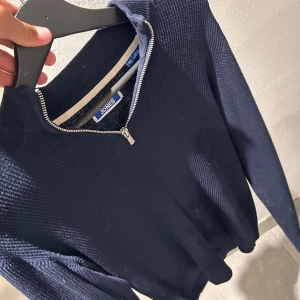 Mörkblå stickad tröja Jack & Jones - Snygg mörkblå stickad tröja från Jack & Jones med half zip-dragkedja vid halsen. Tröjan har långärmad passform och är perfekt för dig som gillar en stilren och enkel look. Ribbad struktur ger extra detalj och komfort.