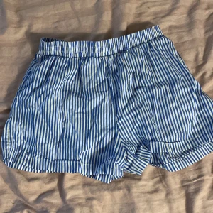Blåvit randiga shorts från FB Sister - Snygga blå och vita randiga shorts från FB Sister i storlek S. De har elastisk midja. Perfekta för varma sommardagar och chill häng. Passformen är loose och de har en klassisk, avslappnad look.