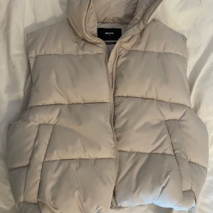 Beige väst från Bik Bok - Snygg beige väst från Bik Bok med hög krage och dragkedja framtill + fickor. Perfekt att slänga över en hoodie nu när det börjar bli lite kallare ute. Endast använd en gång 