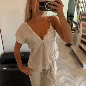 Assymterisk topp/blus från zara  - Säljer en drömmig topp/blus med v-ringning och spetskant vid bysten. Toppen har ett axelband och en kort ärm, samt knyt i sidan för extra detalj. Materialet är lätt och har ett subtilt blommigt mönster. Använd 1 gång o är i nyskick🥰