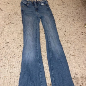 Blå bootcut jeans med slitna detaljer - Säljer ett par ljusblå bootcut jeans med klassisk femficksdesign och slitna detaljer på bakfickan. Jeansen har en snygg utsvängd passform och är tillverkade i mjukt denimtyg. Perfekta för dig som gillar retrovibbar och vill sticka ut.