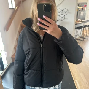 Svart pufferjacka från Vila, stl 34 - Säljer en svart pufferjacka från Vila i storlek 34. Jackan har hög krage, två fickor framtill och den är matt! 